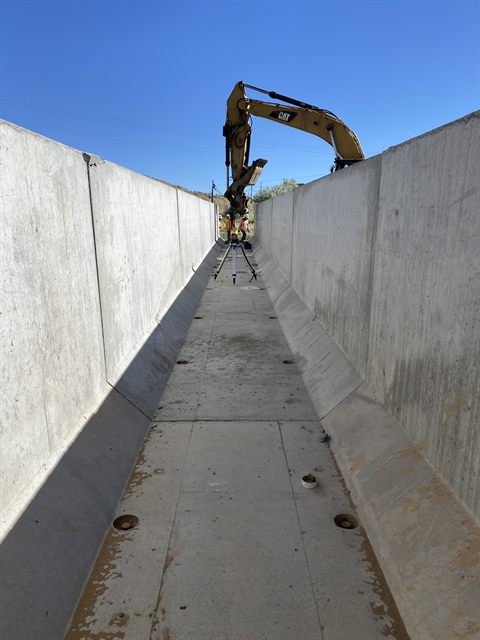 A finished cast-in-place concrete drainage channel, with an excavator working above the wall.