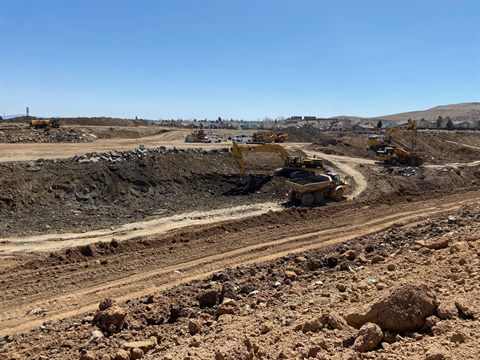 Excavators and articulated haulers working a wide mass excavation, dozers cutting the bench above.